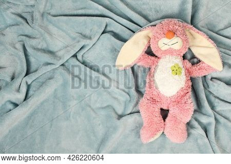 A Plush Bunny Toy Sitting On Plush Blanket And White Wall. Plush Pink Bunny Toy With Pink Knitted Oc