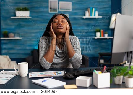 Worried Displeased African Student Suffering Headache Migraine Sitting At Desk Table In Living Room.
