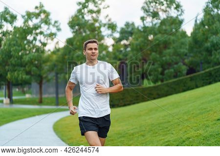 Attractive Man Athlete Wearing Sportswear Run In Modern Park At Summet
