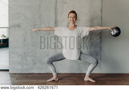 Happy Fit Redhaired Woman Sits In Plie In Second Position With Small Fitball In One Hand And Does Ba