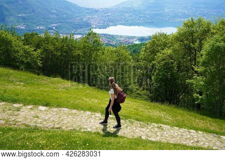 Female Hiker Walks The Trail And Looks With Satisfaction From The Top Of Mountain The Lake