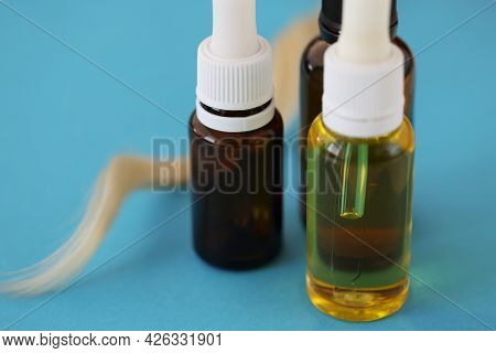 Many Jars Of Cosmetic Oil Standing Near Lock Of White Hair On Blue Background Closeu