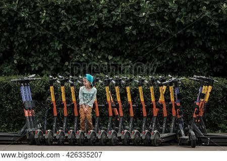 Moscow, Russia - July 3 2021: A Child Stands In The Parking Lot Of Electric Scooters