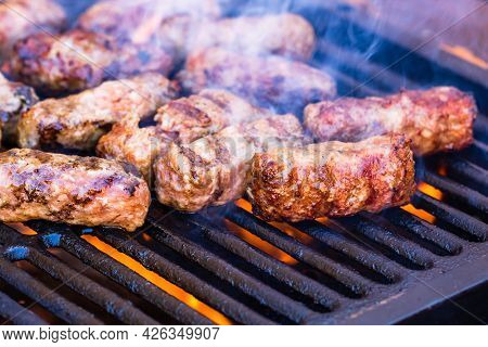 Preparing Meat Rolls Called Mici Or Mititei On Barbecue. Close Up Of Grill With Burning Fire With Fl