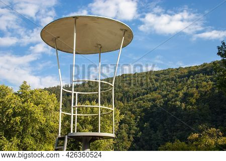 Empty Old Metal Lifeguard Seat At A Public Swimming Pool In Germany In Front Of A Green Forrest Back