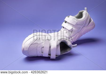 Two White Kid Running Shoes With Velcro Fasteners For Easy Childrens Footwear, Isolated On A Purple 