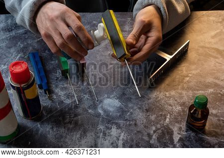 Pour Oil Onto A Whetstone. The Knifemaker Is Holding Oil And A Sharpener. The Hands Of The Master. F