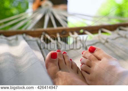 Woman Legs With Red Nail Polish On Hammock. Woman With Beautiful Pedicure Resting On Hammock At Sunn