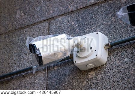 New Surveillance Camera In A Plastic Bag Are Mounted On A Wall Of Stone. Connected By Wires.