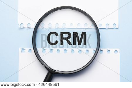 Magnifying Glass Loupe With Sign Crm Between Two Paper Sheets On The Blue Table.