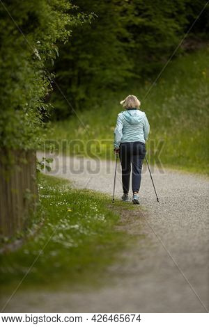 An elderly woman in nature Nordic walking outdoors. Healthy daily cardio routine.