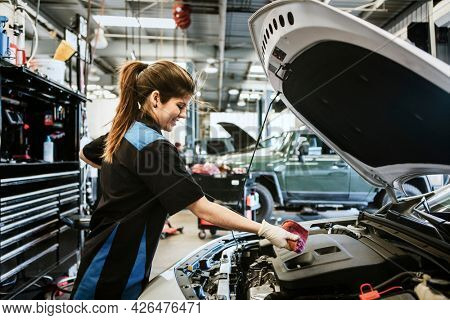 Young female mechanic wiping the engine oil dipstick