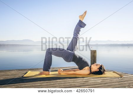 Una imagen de una linda mujer haciendo yoga en el lago - Setu Bandha