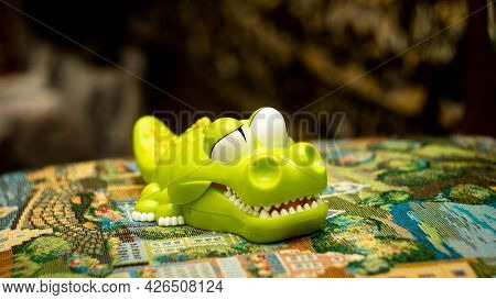 A Plastic Crocodile Toy Lying On A Chair Against A Blurry Background.