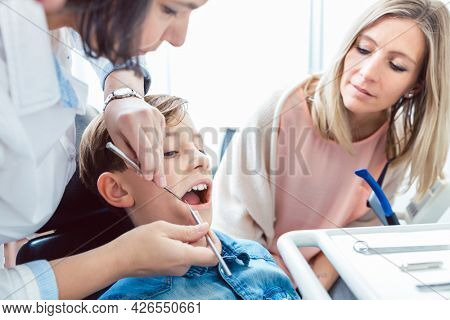 Patient's mother looking at her son examining teeth by dentist
