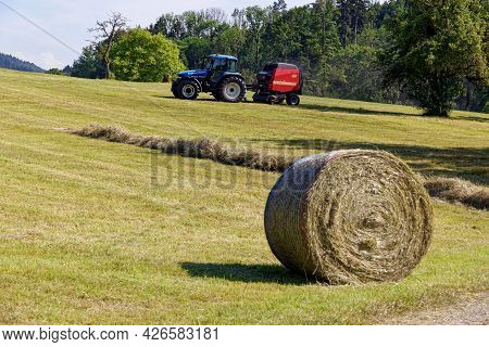 Aadorf, Switzerland June 17, 2021 Blue Tractor With Red Trailer On A Field, Farm Machinery Harvestin