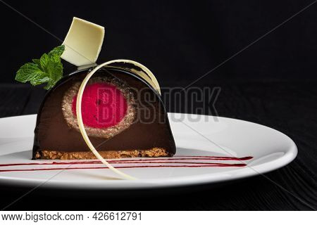 Delicious biscuit chocolate cake closeup with pink souffle decorated with mint and white chocolate on dark background