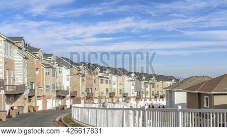 Pano Townhouses Along Road With White Fence Against Scenic Blue Sky And White Clouds