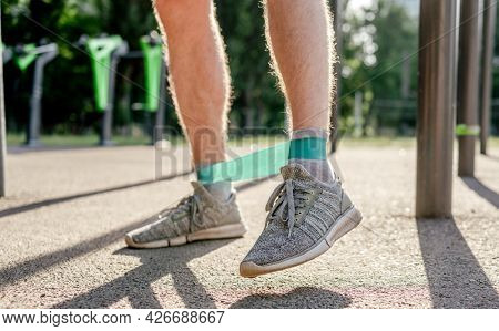 Closeup side view of legs feets of man guy training with elastic rubber band at the stadium outdoors. Athlete adult male person during active workout with additional sport equipmant