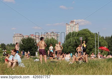 Moscow, Russia - July 2021: Crowd Of People Sunbathing On A Green Lawn On Background Of Residential 