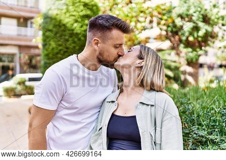Young caucasian couple of boyfriend and girlfriend having fun outdoors on a un sunny day kissing in love