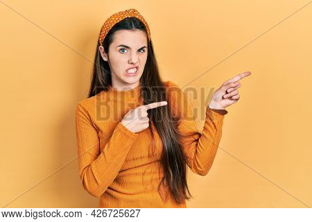 Young brunette teenager wearing casual yellow sweater pointing aside worried and nervous with both hands, concerned and surprised expression 