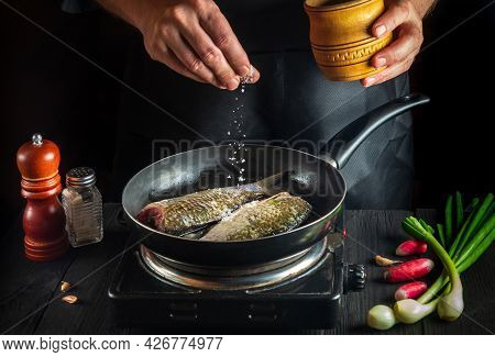Professional Chef Prepares Fresh Fish In Pan Sprinkling Salt With The Ingredients. Preparing To Cook
