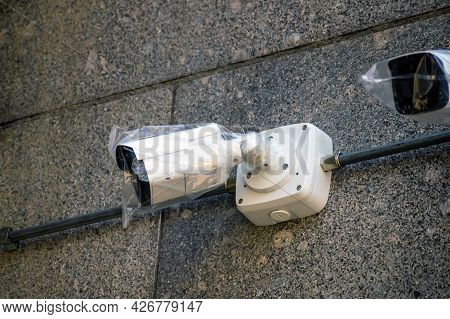New Surveillance Camera In A Plastic Bag Are Mounted On A Wall Of Stone. Connected By Wires.