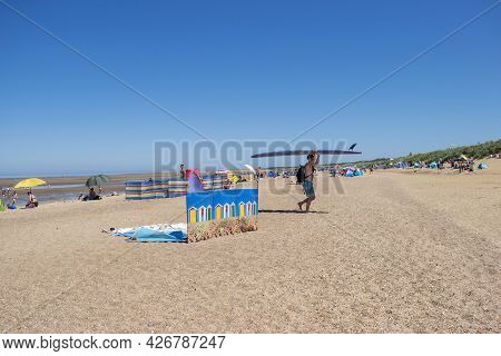 Old Hunstanton, Norfolk, England - June 13, 2021. Windbreaker And Man Carrying A Surfboard At Old Hu
