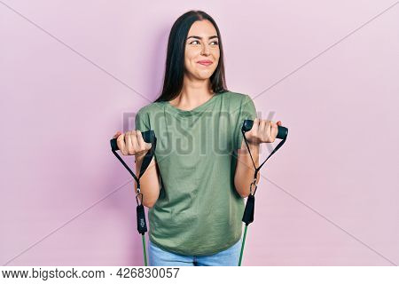 Beautiful woman with blue eyes training arm resistance with elastic arm bands smiling looking to the side and staring away thinking. 