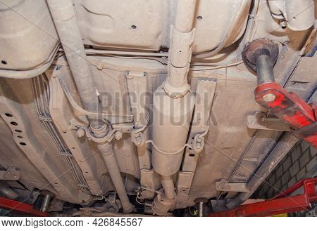 Bottom View Of The Underbody Of An Old Car On A Lift. In The Garage, A Man Changes Parts On A Vehicl