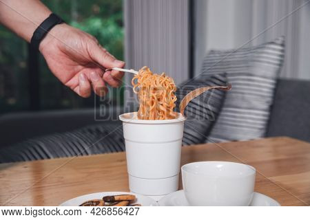 Hand Of A Man Holding A Plastic Fork With Cooked Instant Noodles. A Cup Of Instant Noodle With Fork 