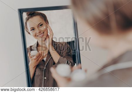 Reflection In Mirror Of Beautiful Woman In Silk Pajama Smiling While Applying Face Cream For Deeper 