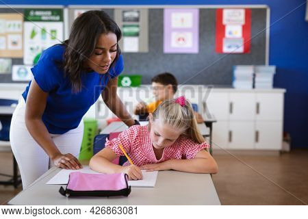 African american female teacher teaching caucasian girl in the class at elementary school. school and education concept