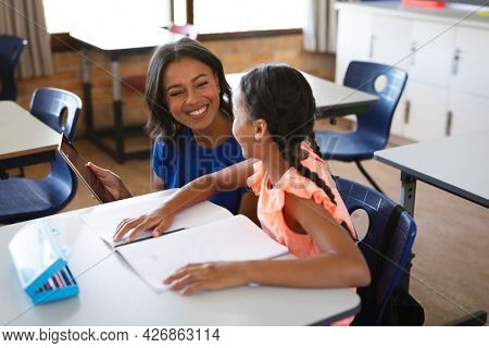 African american female teacher with digital tablet teaching a girl at elementary school. school and education concept