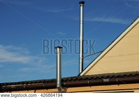 Two Gray Metal Chimney Pipes On The Brown Roof Of A Private House Against A Blue Sky