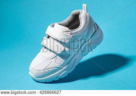 Macro Flying White Child Sneakers With Velcro Fasteners Isolated On A Blue Background With Hard Ligh