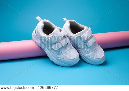 The Composition Is A Balance Of Two White Childrens Sneakers With Velcro Fasteners For Easy Footwear