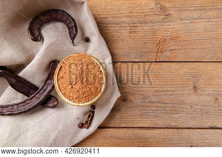 Dry Carob Pods And Carob Powder On Linen Napkin Over Wooden Background