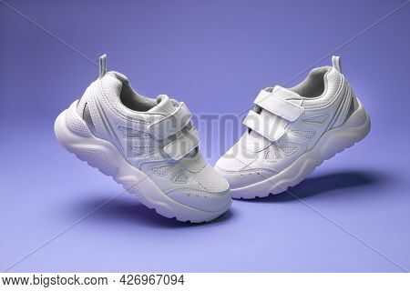 Side View White Unisex Sneakers With Velcro Fly In The Air Toes To Each Other Isolated On Purple Bac