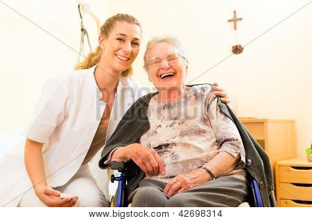 Infermiera giovane e femminile senior in casa di cura, la vecchia signora seduta in una sedia a rotelle