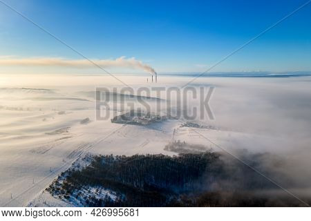 Aerial View Of Winter Landscape With Foggy Countryside And Distant Factory Pipes Emmiting Black Dirt