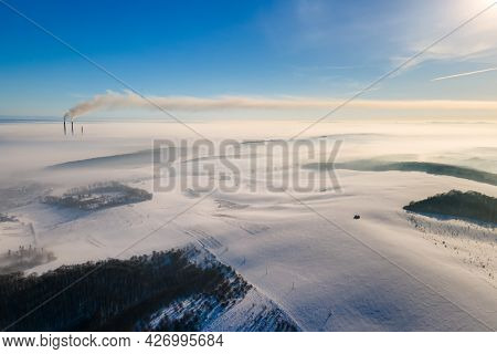 Aerial View Of Winter Landscape With Foggy Countryside And Distant Factory Pipes Emmiting Black Dirt