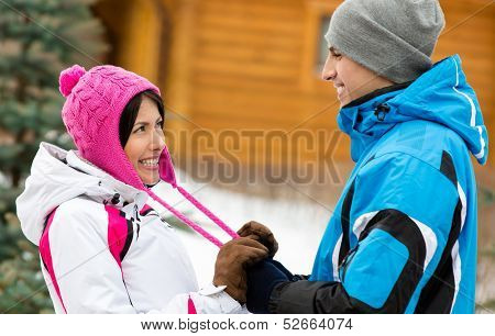 Half-length portrait of man and woman looking at each other who wear warm caps and jackets during winter holidays