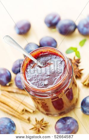 Fresh homemade plum butter in a jar with spoon, plums and spices