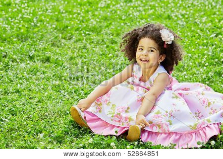 Little  girl sits on grassy lawn spreading hem of her dress