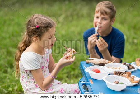 Boy and girl eat meat with vegetables at the picnic on pembroke table