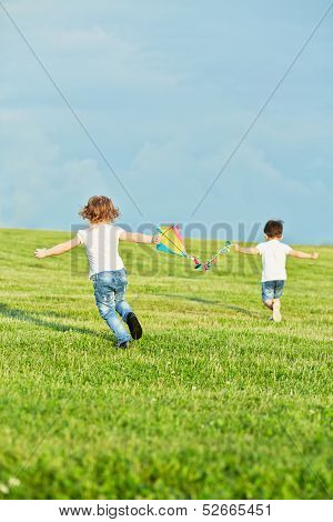 Little girl and boy run on meadow to fly kite, rear view, focus on girl