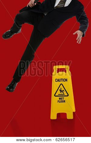 Businessman slipping on wet floor in front of caution sign over red background