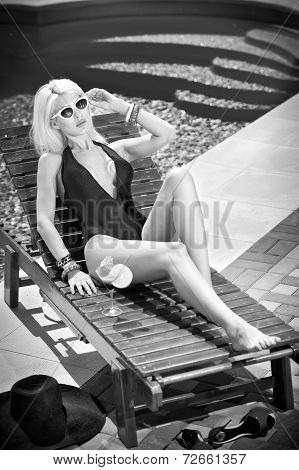 Beautiful sensual blonde with fashionable sun glasses relaxing at swimming pool with a juice